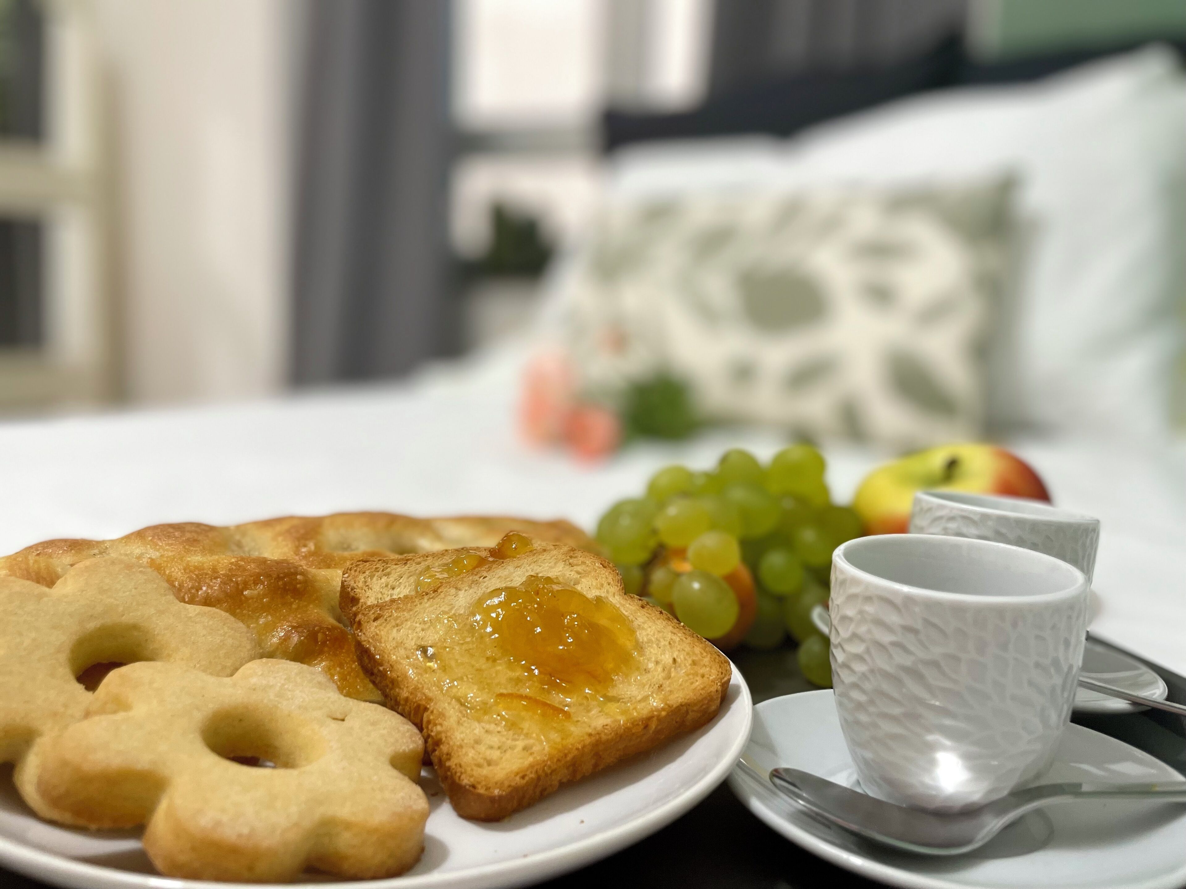 A breakfast setting with toast, cookies, grapes, and a cup on a plate.