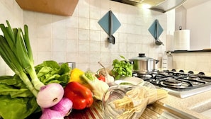 A kitchen with a stove, a pot, and various vegetables like onions, bell peppers, and leafy greens on the counter. - Happy Family Apartments Andreana (Genoa)