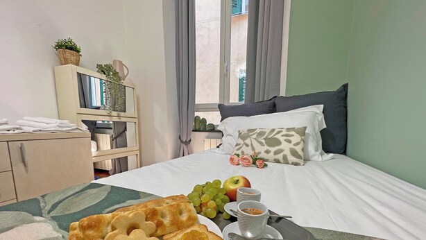 A neatly made bed with a tray of breakfast items including toast, grapes, an apple, and a cup of coffee. - Happy Family Apartments Andreana (Genoa)