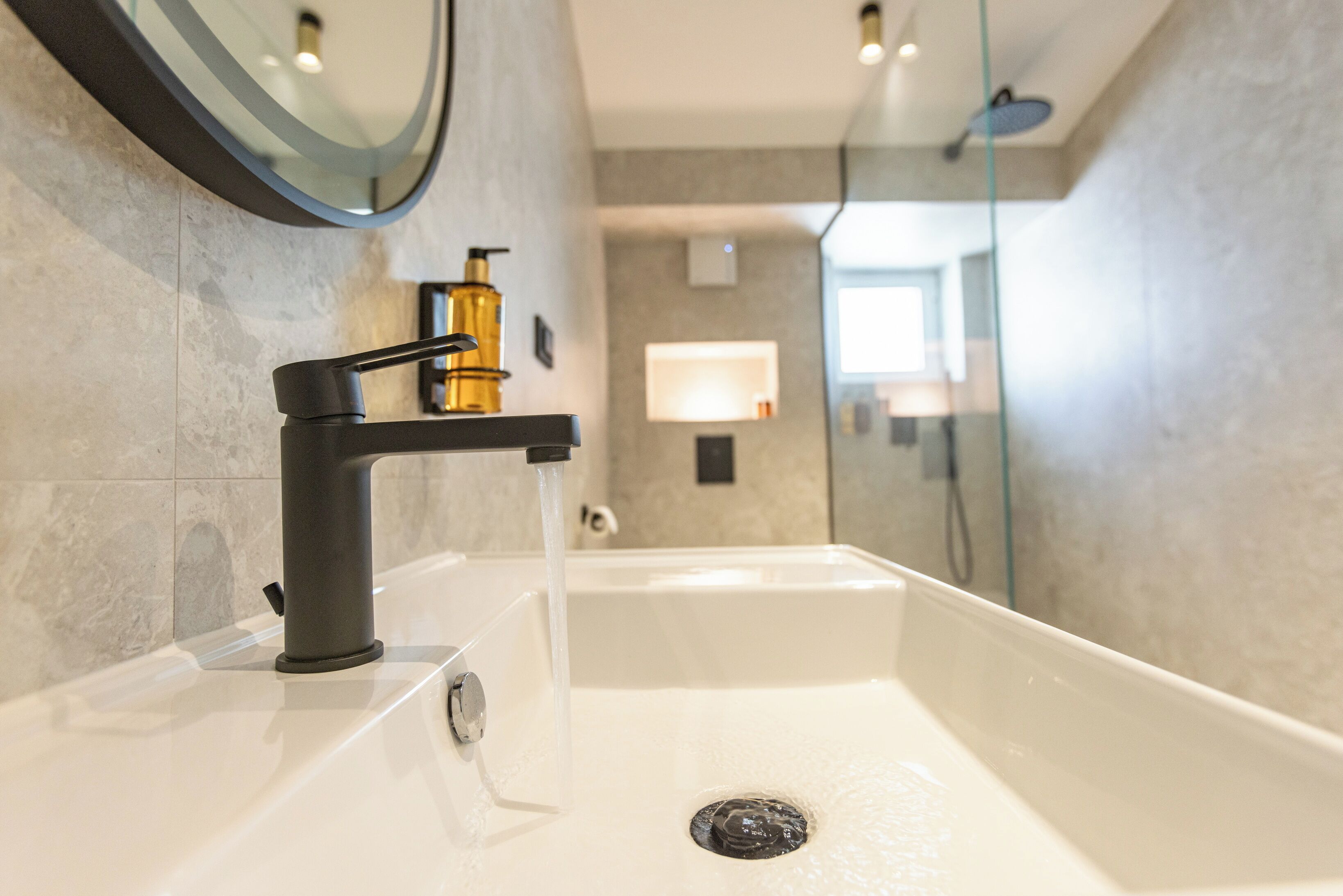 A modern bathroom with a white sink, black faucet, and a gold soap dispenser.