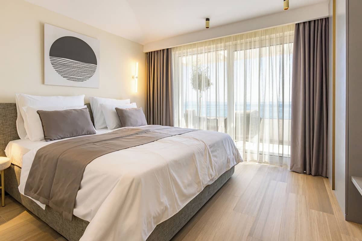 Une chambre d’hôtel moderne avec un grand lit, une vue sur la mer et un balcon agrémenté de rideaux.
