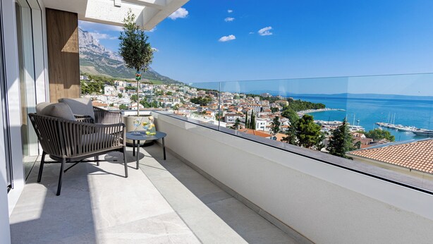 A balcony with a view of a coastal town, a table with a chair, and a potted plant.