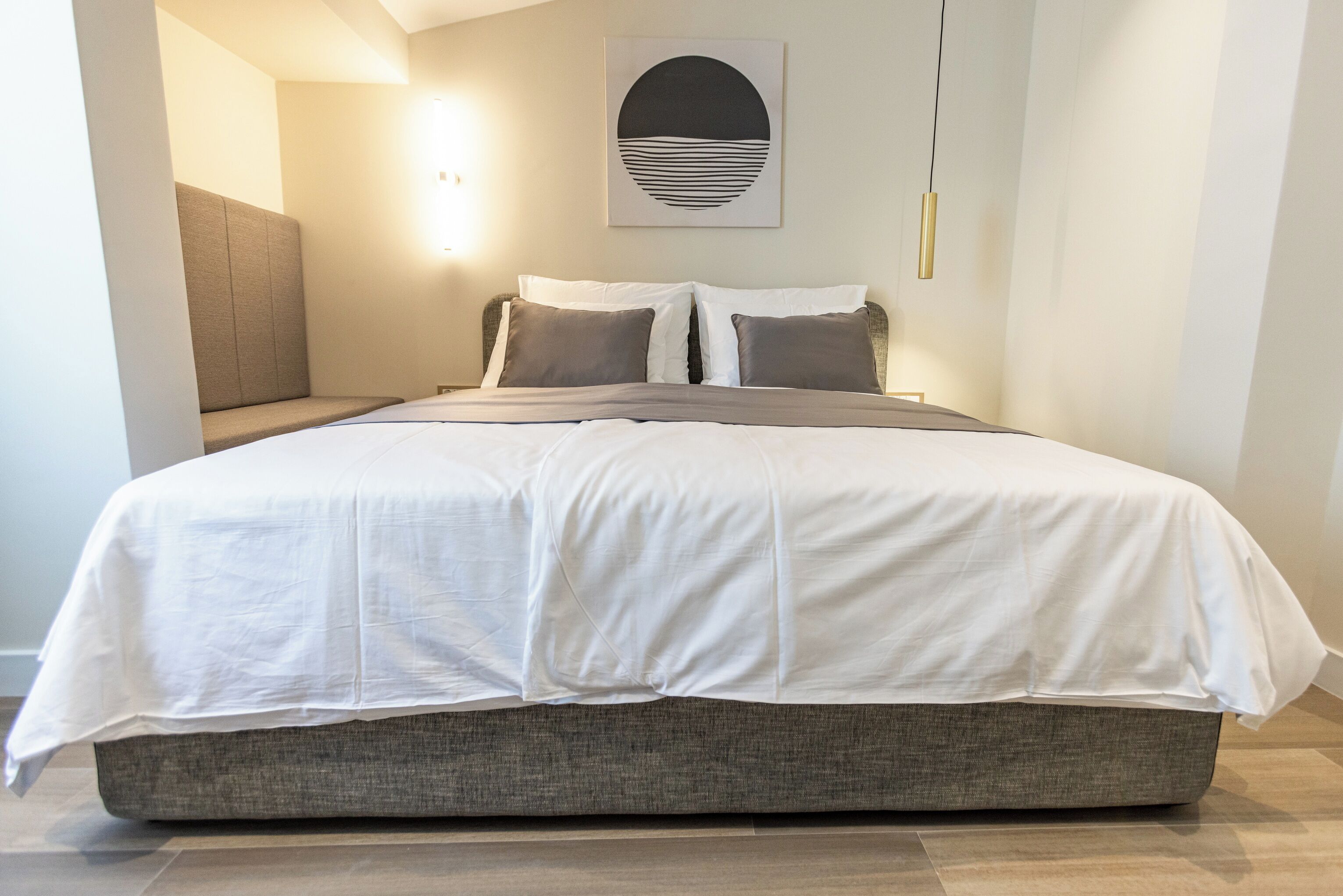 A modern bedroom with a large bed, grey upholstered headboard, and a wall-mounted artwork.