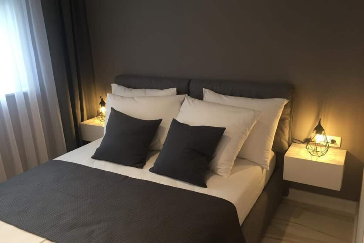 Un lit bien fait, recouvert d’une couvre-lit noir et blanc, avec deux oreillers noirs et une tête de lit blanche. Deux tables de chevet avec des lampes sont placées de chaque côté du lit.