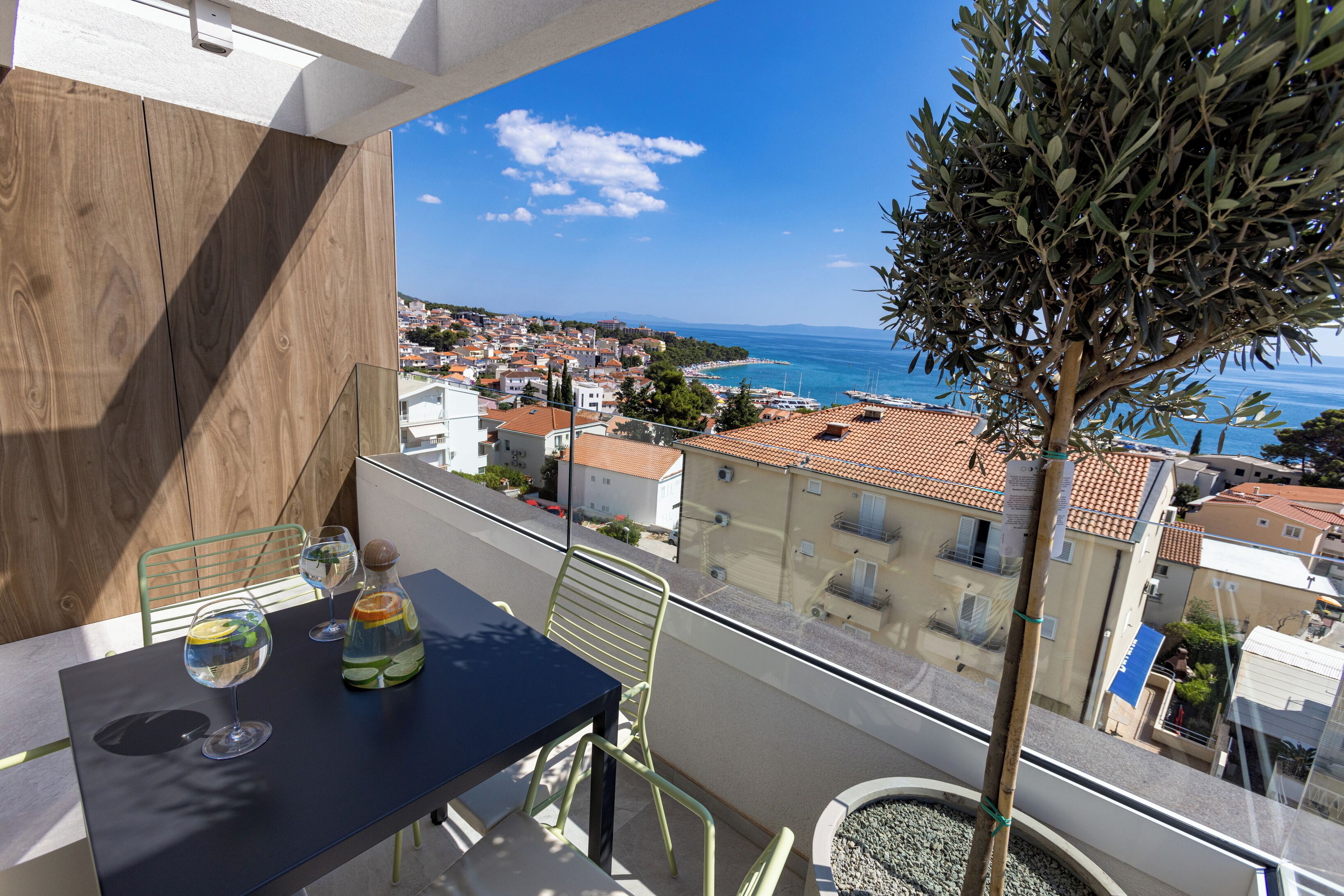 A balcony with a table, chairs, and a view of the sea and town.