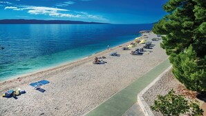A beach with clear blue water, a paved walkway, and several umbrellas.