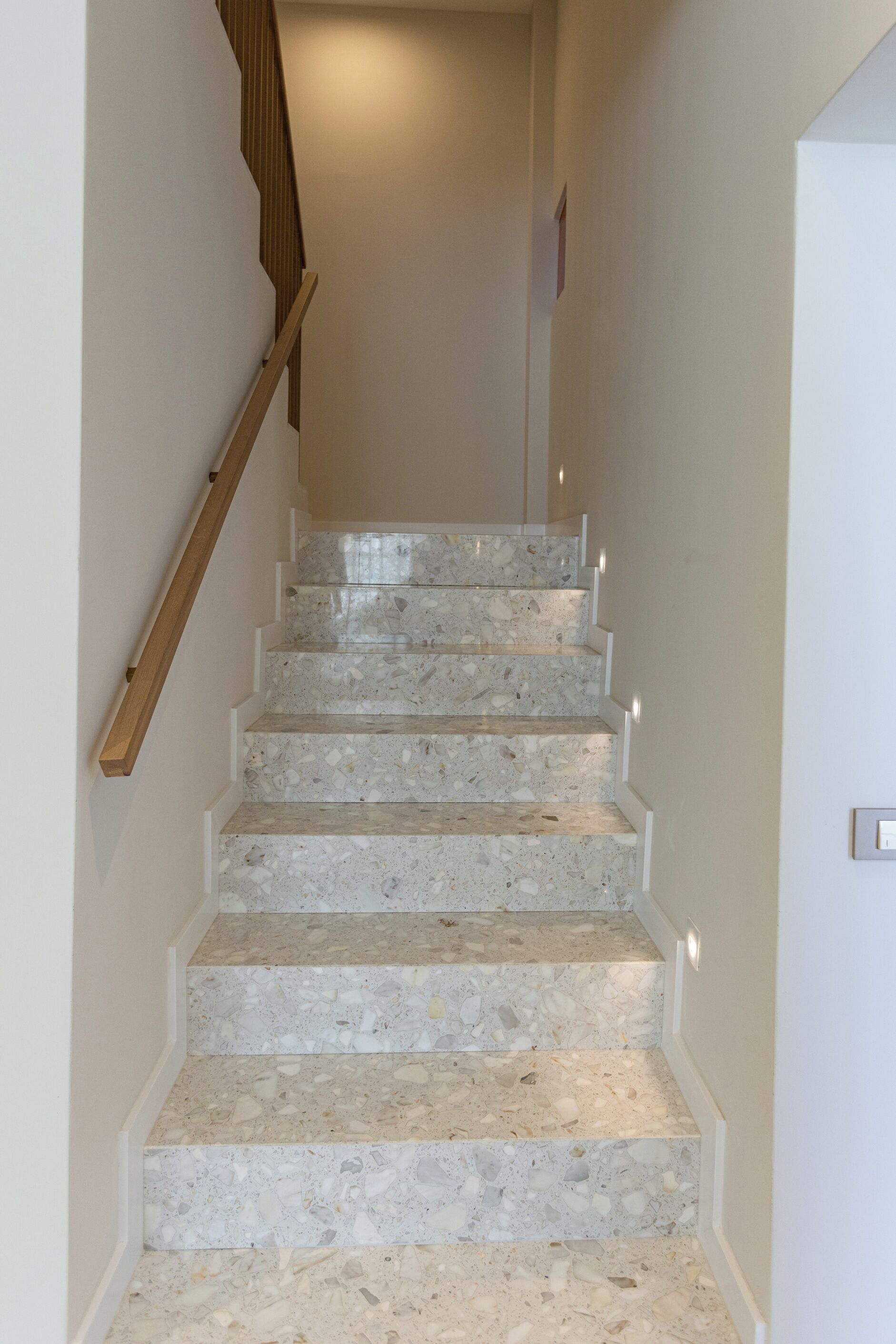 A staircase with a wooden handrail and white walls.