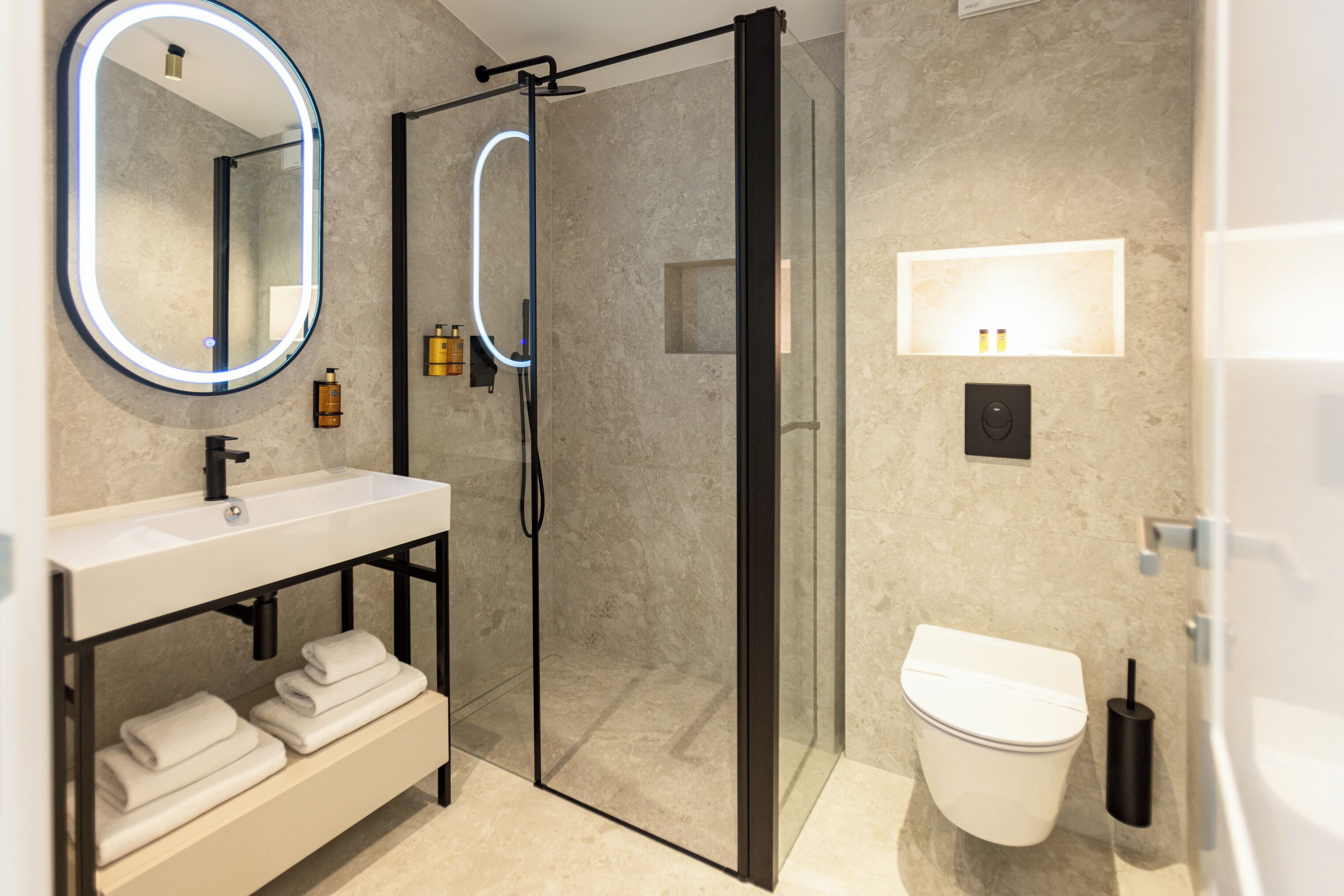 A modern bathroom with a glass-enclosed shower, a white sink with a black faucet, and a toilet with a black flush handle.