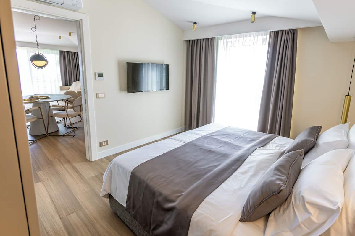 Une chambre d’hôtel moderne dotée d’un grand lit, d’un téléviseur à écran plat fixé au mur et d’un coin repas avec une table et des chaises.