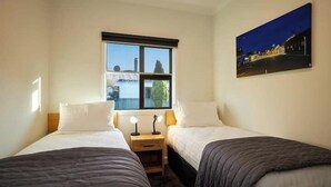 Ein Schlafzimmer mit zwei Betten, einem Fenster, einem Nachttisch mit Lampen und einem Gemälde an der Wand.