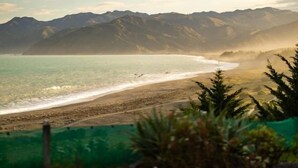 Eine Küstenlandschaft mit Bergen im Hintergrund, einem Sandstrand und etwas Grün im Vordergrund.