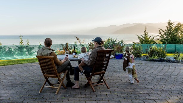 Eine Familie speist draußen mit Blick auf das Meer und die Berge.