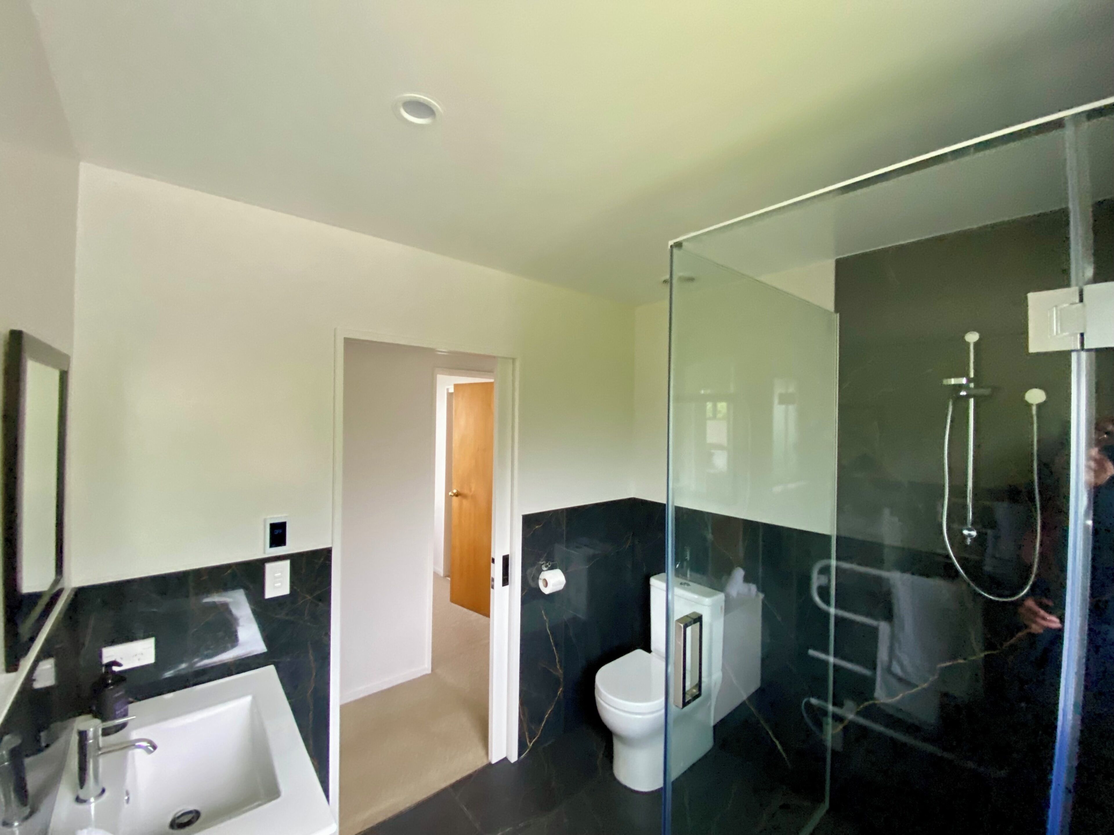 Un baño moderno con ducha de vidrio, inodoro blanco y lavamanos con encimera negra.