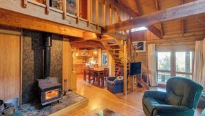 En rummelig opholdsstue med en stenspir, træbjælker og en trappe til en etage over.