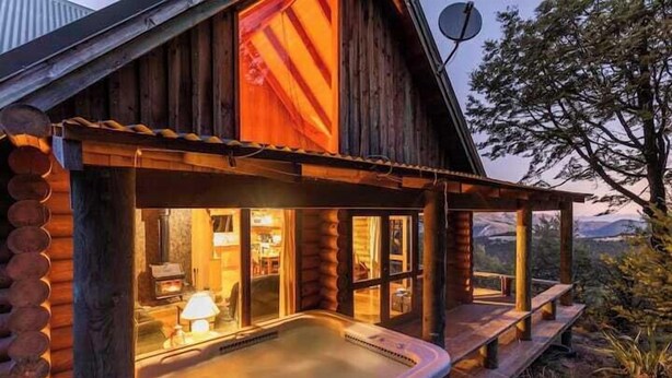 En træhytte med jacuzzi, træfacade og udsigt til bjerge.