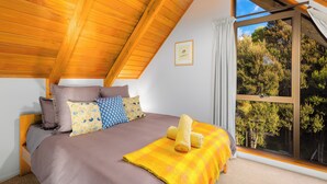 A bedroom with a large window, wooden ceiling beams, and a bed with multiple pillows and a blanket. - Totara Lodge | Snow | Couple Retreat - ML97564 (Mount Lyford Village)