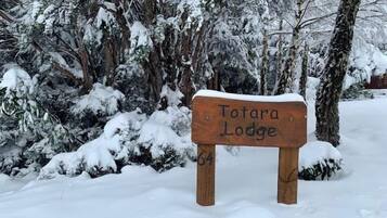 A wooden sign with 'Totara Lodge' written on it, surrounded by snow-covered trees.