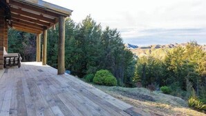 Una terraza de madera con una pérgola, con vistas a un paisaje montañoso de bosque denso.