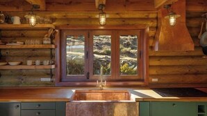 Una cocina rústica con paredes de madera, un lavamanos de cobre y un ventanal con vistas a terreno rocoso.