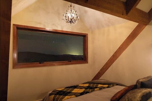 Un dormitorio con un ventanal grande, una araña y una cama con manta a cuadros.
