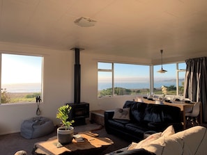 A living room with a fireplace, a sofa, a dining table, and large windows overlooking a scenic view.