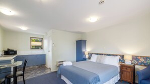 Hotellihuone, jossa on sänky, työpöytä tuolilla, mikroaaltouuni, pieni kaappi ja yöpöytä lampulla.