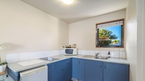 Eine Küche mit blauen Schränken, einer Mikrowelle, einem Spülbecken und einem Fenster mit Blick ins Grüne.