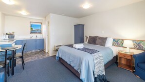 Ein kleines Hotelzimmer mit Bett, Nachttisch und einer kompakten Küchenzeile.