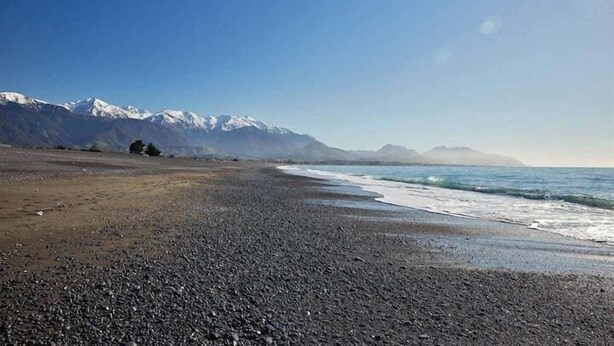 Ein Kiesstrand mit Blick auf schneebedeckte Berge in der Ferne.