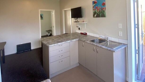 A compact kitchen with a countertop, sink, and cabinets. There is a television mounted on the wall and a painting above it. - Waterfront | Handy Location | Affordable | Unit 7 - KK41647 (Kaikoura)