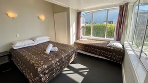 Quarto de hotel com duas camas, um guarda-roupa, uma janela com cortinas e uma luminária no teto.