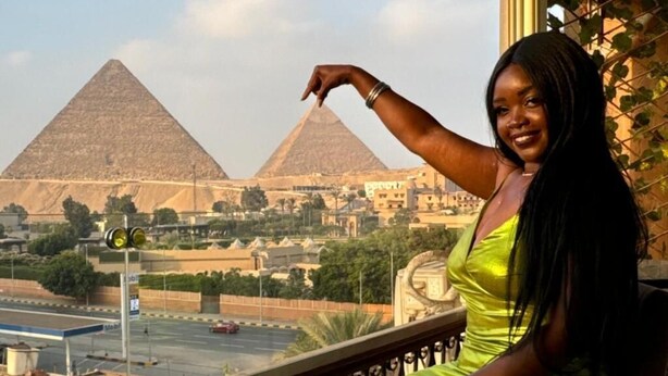 Une personne assise sur un balcon, d’où l’on peut admirer les pyramides.