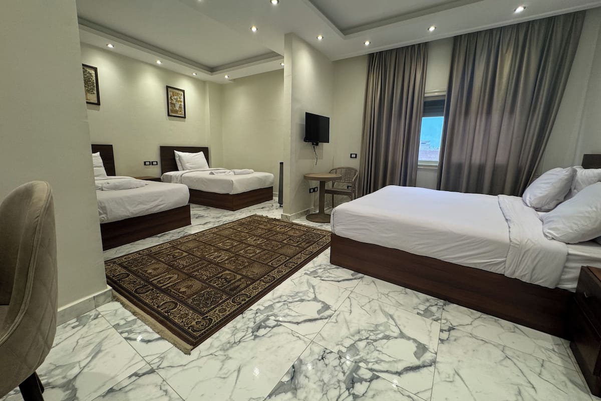 A hotel room with two beds, a sitting area, a TV, and a view of the outdoors.