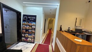 Un hall d’accueil d’hôtel avec un tapis rouge, un comptoir de réception et une affiche murale faisant la publicité des visites guidées proposées par l’hôtel.