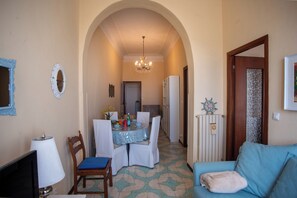 A dining area with a table set for four, a chandelier, and a blue sofa with a cushion.