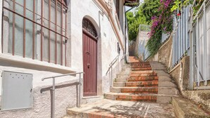 Un escalier étroit menant à un bâtiment doté d’une porte rouge et de fenêtres grillagées.