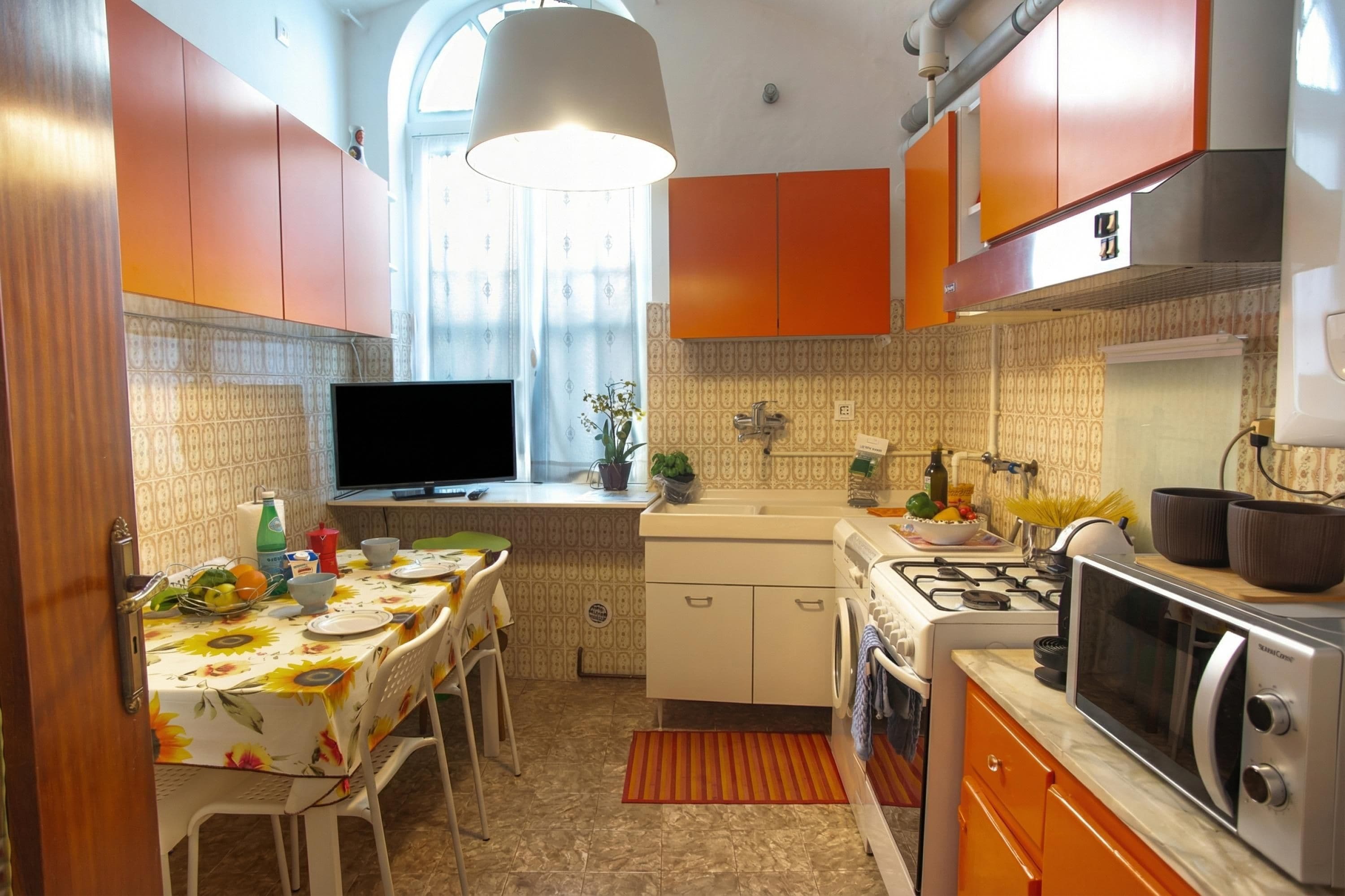 Une cuisine compacte avec un coin repas, un téléviseur et une fenêtre avec des rideaux.