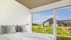 Une chambre à coucher moderne avec un grand lit, un plafond en bois et une porte-fenêtre coulissante donnant sur un jardin.