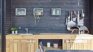 Une cuisine extérieure en bois, dotée d’un évier encastré, de plantes en pot et d’un four à pizza.