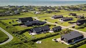 Un quartier résidentiel en bord de mer, avec des maisons modernes, de vastes pelouses verdoyantes et une vue dégagée sur la mer.