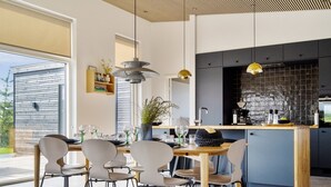 Une cuisine moderne dotée d’un îlot central, de grandes fenêtres et d’un coin repas avec des chaises et une table.
