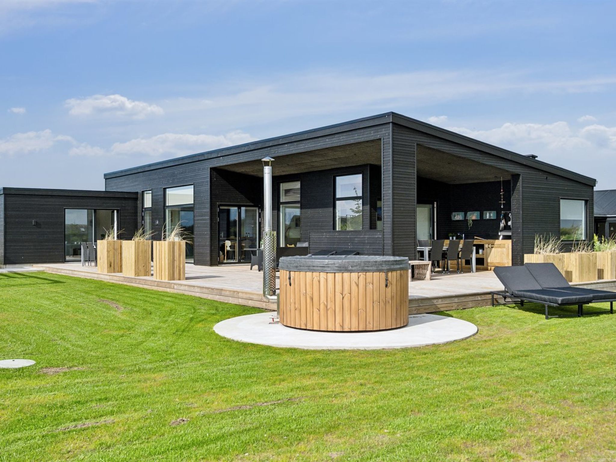 A modern building with a covered patio area, outdoor seating, and a circular wooden structure.