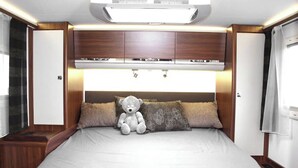Un dormitorio con una cama, un osito de peluche, armarios de madera y una ventana.
