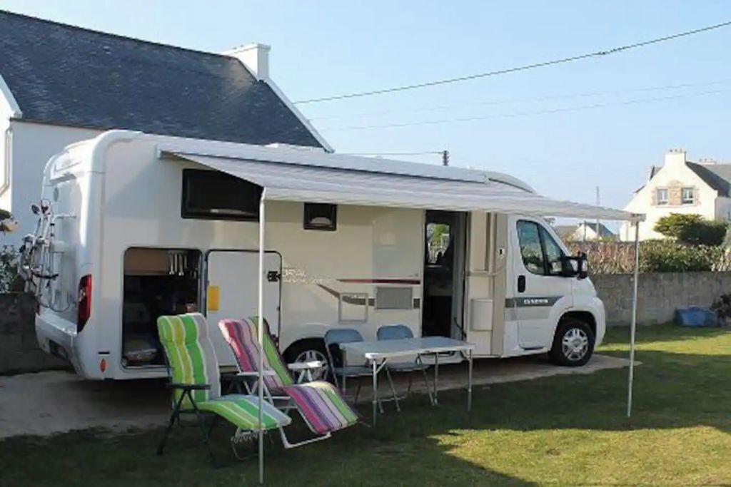 Ein weißer Campervan mit einer überdachten Terrasse, einem Tisch und zwei gestreiften Lounge-Stühlen.