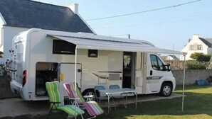 Una camper blanca con un porche cubierto, una mesa y dos sillones a rayas.