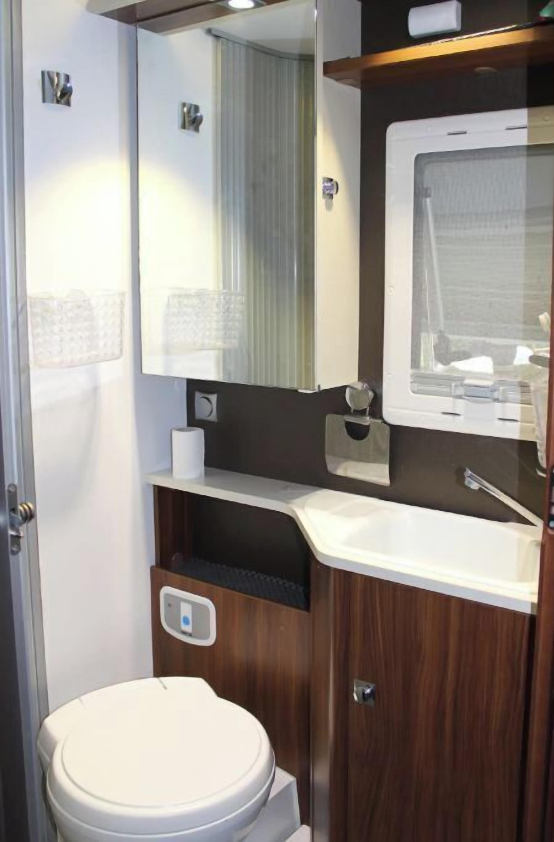 Ein kleines Badezimmer mit Toilette, Waschbecken, Spiegel und Fenster.