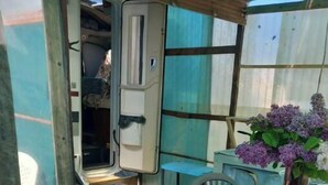 Un espacio exterior pequeño y cerrado con una mesa cubierta con un mantel azul y blanco de estampado de hojas, un jarrón con flores moradas y una hogaza de pan.