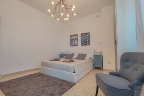 Une chambre à coucher comprenant un lit, une chaise, un tapis, une table de chevet, une lampe et un luminaire au plafond.