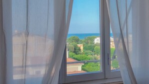 Ein Fenster mit durchscheinenden Vorhängen, Blick auf eine Wohngegend und einen klaren Himmel.