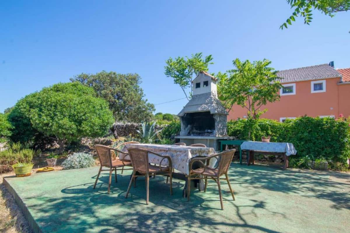 An outdoor patio with a table and chairs, a stone barbecue grill, and a building in the background.